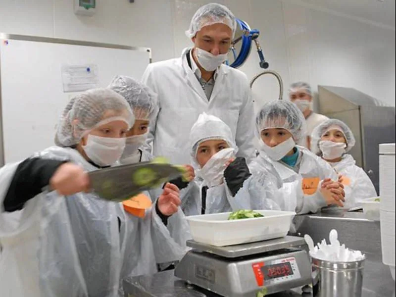 Atelier pédagogique en cuisine collective, enfants en charlotte et blouse pesant des légumes sur une balance B3C inox