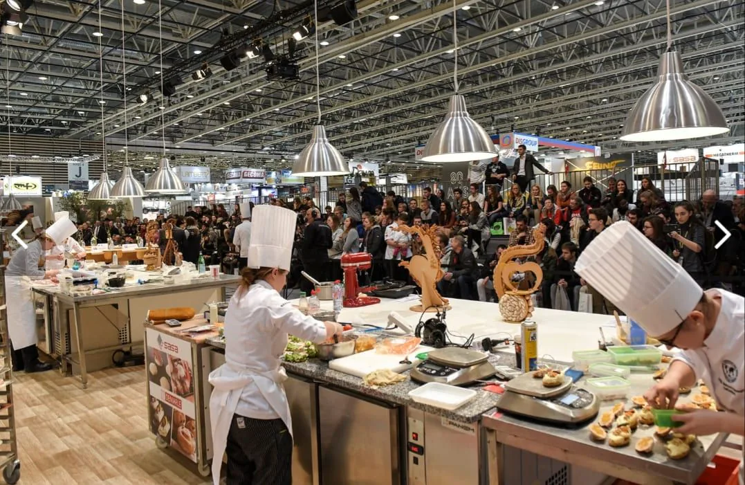 Stand de démonstration culinaire avec chefs en toque et balances B3C sur les plans de travail lors d'un salon professionnel